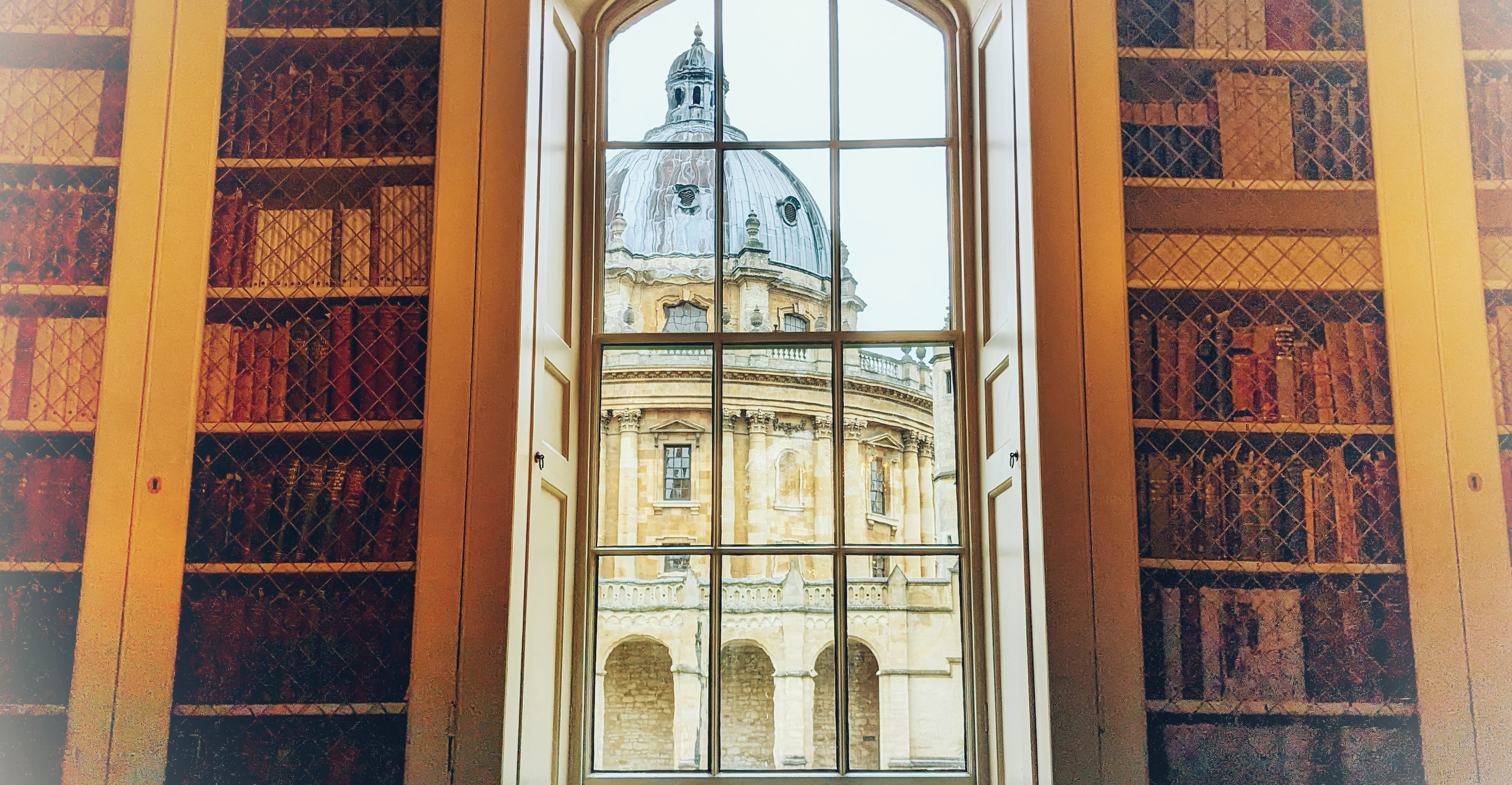 A view of the Radcliffe Camera through a window with bookshelves either side.