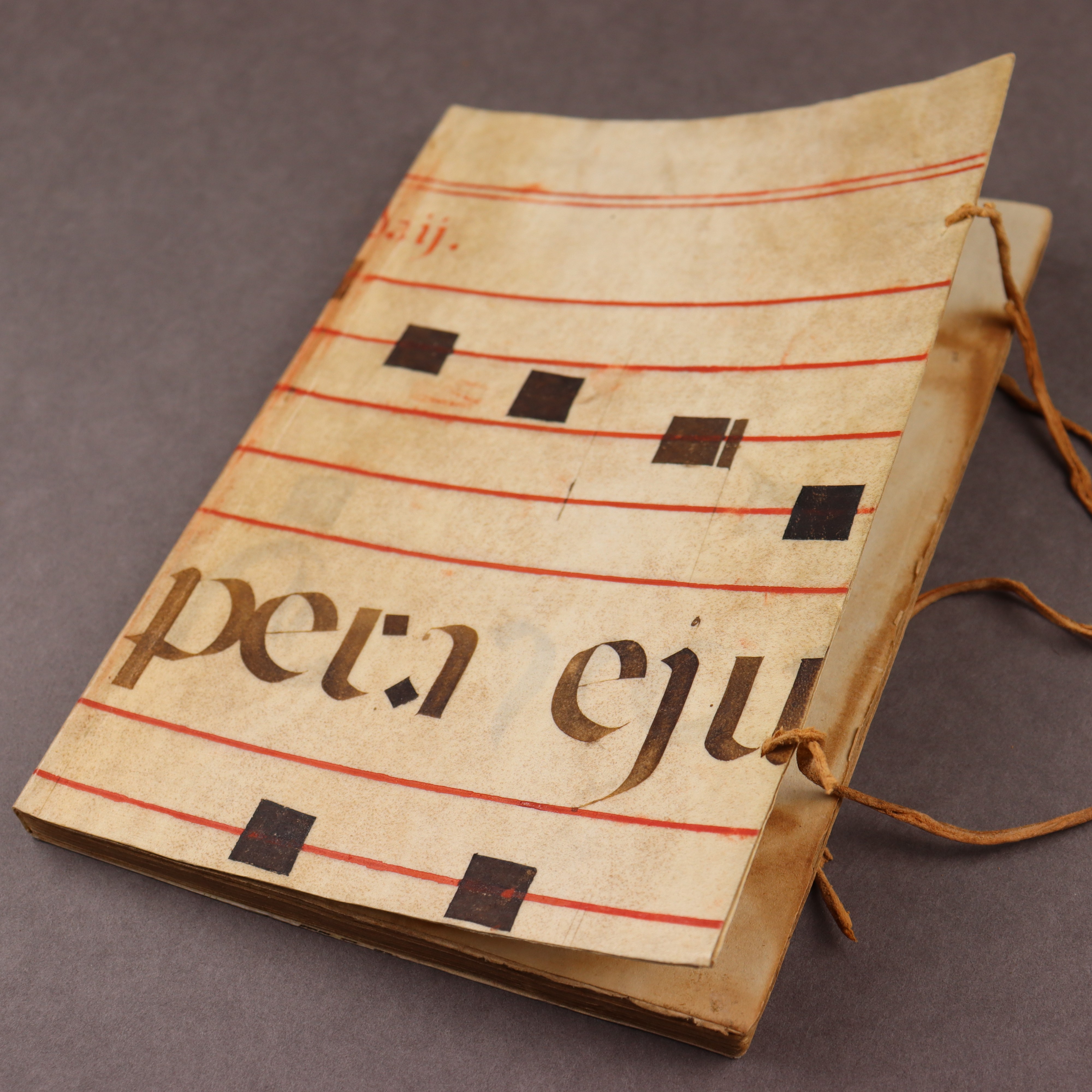 The cover of a slim volume bound in parchment cut from a  music manuscript in red and black ink.
