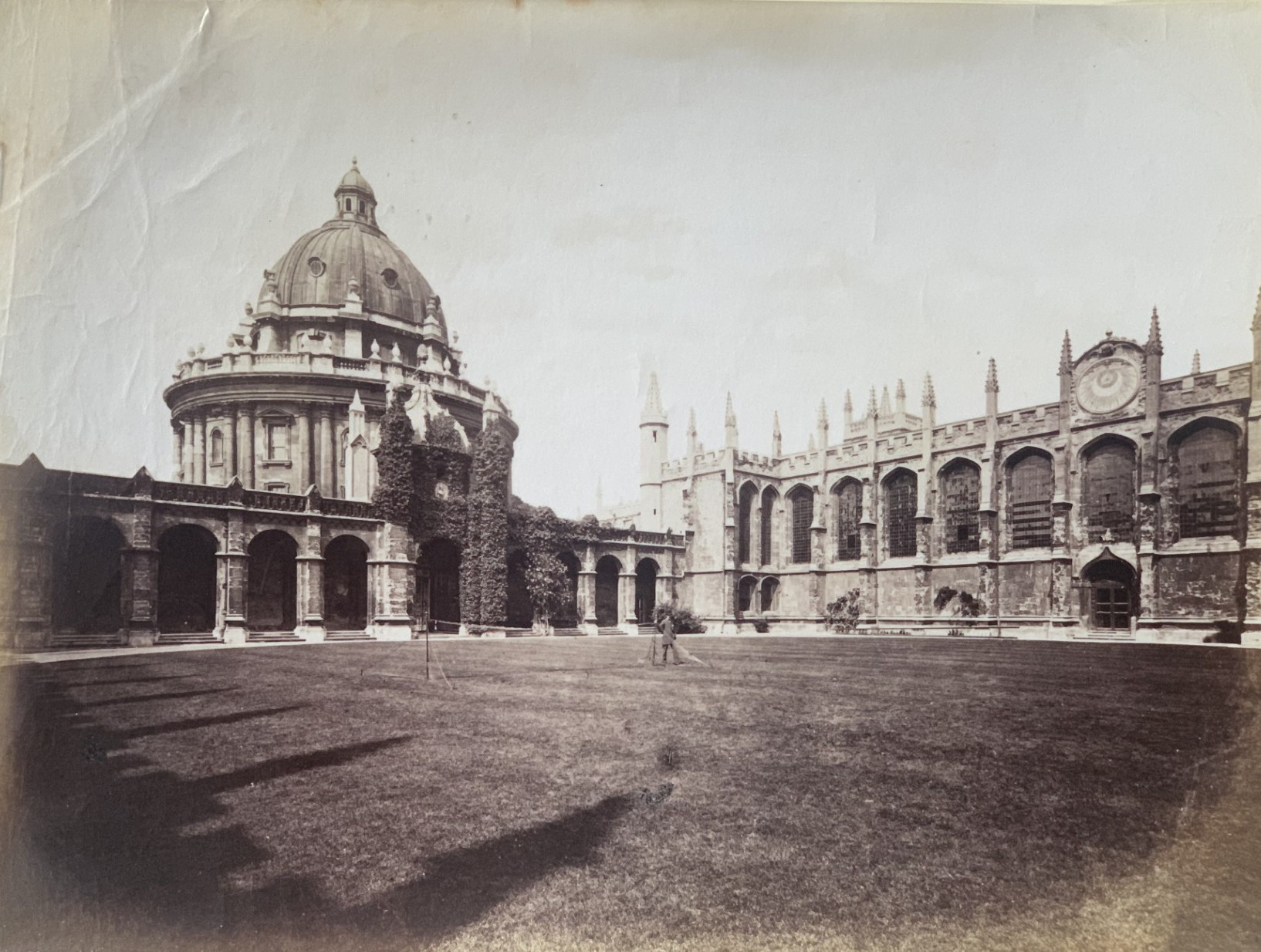 A black and white photograph of the Great Quad at All Souls College facing towards the Library and Radcliffe Camera, a tennis net is set up in the centre of the quad