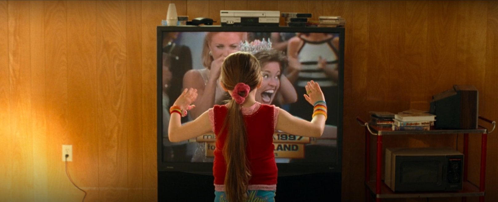 A still from the movie Little Miss Sunshine. A young girl faces a television on which a beauty pageant is being shown.