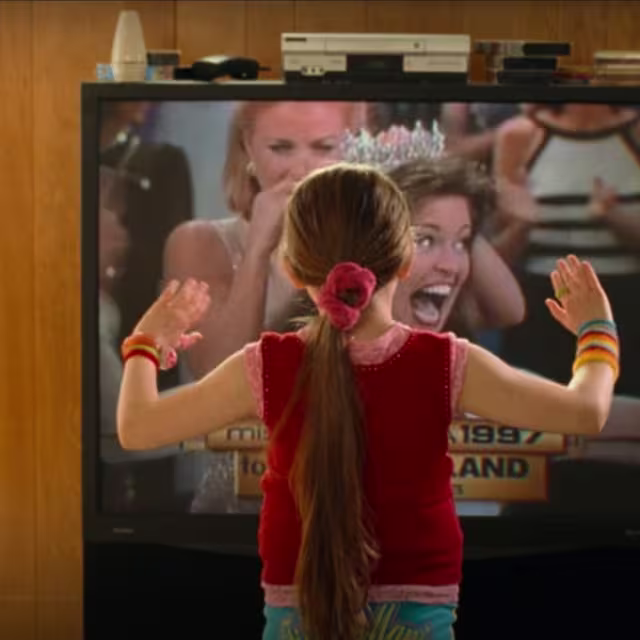 A still from the movie Little Miss Sunshine. A young girl faces a television on which a beauty pageant is being shown.