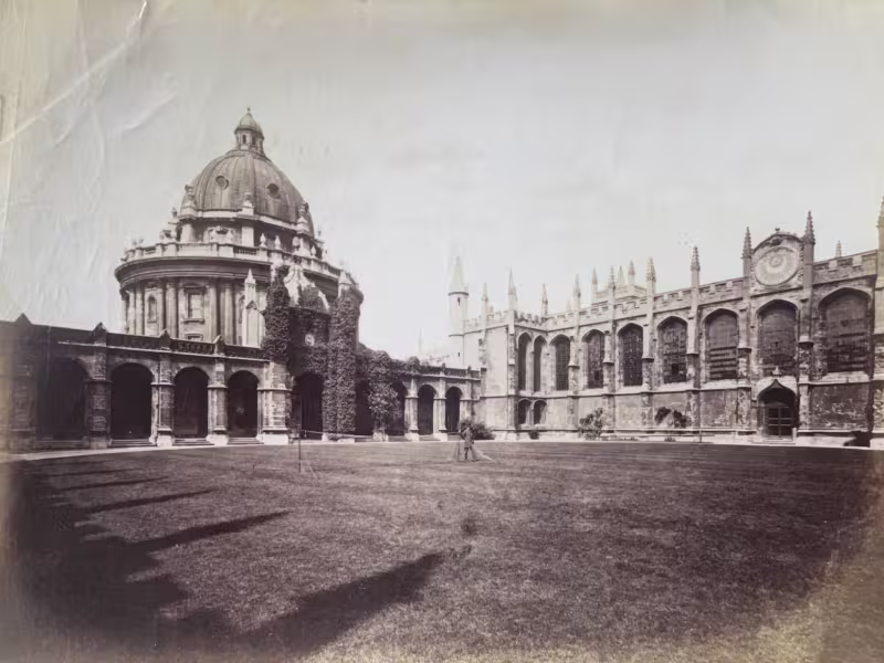 A black and white photograph of the Great Quad at All Souls College facing towards the Library and Radcliffe Camera, a tennis net is set up in the centre of the quad